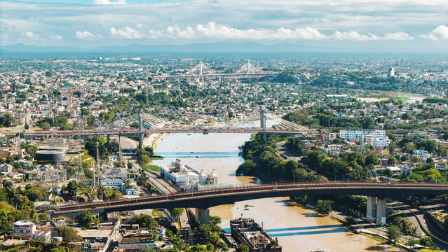 Aerial view of Rio Ozama with multiple bridges spanning the river and dense city buildings under a bright sky in Santo Domingo, DN, Dominican Republic.