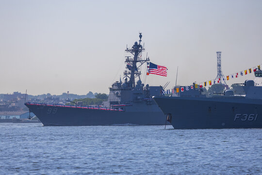 Jersey City, New Jersey, United States - 04 July 2026: View of two naval warships sailing on the water with signal flags and the American flag flying under a clear sky.