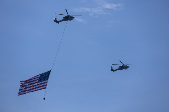Jersey City, New Jersey, United States - 04 July 2026: View of two military helicopters flying in formation against a clear blue sky, one carrying a large American flag over Liberty State Park.