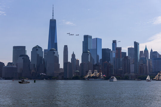 Jersey City, New Jersey, United States - 04 July 2026: View of the Manhattan skyline from Liberty State Park with tall ships on the Hudson River and a jet flyover against a clear blue sky.