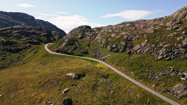 Aerial view of the winding road near Bladalsvatnet surrounded by rocky mountains and green hills in Kvinnherad Municipality, Vestland, Norway.
