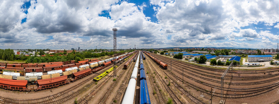 Aerial view of freight trains parked on multiple tracks in a large railway yard with industrial buildings under a blue sky in Novi Sad, Vojvodina, Serbia.