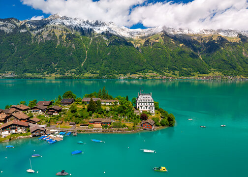 Aerial view of a village on the shore of a turquoise lake with snow-capped mountains in the background and small boats moored at the docks in Interlaken, Canton of Bern, Switzerland.