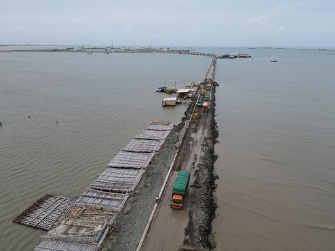 Aerial view of the Patimban port causeway construction site with trucks and building materials extending into the sea in Pusakanagara, West Java, Indonesia.