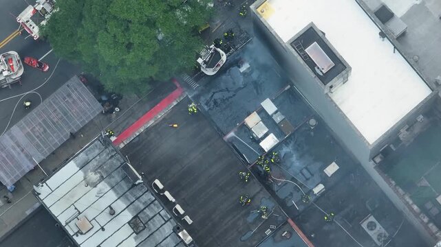 Aerial view of firefighters battling a fire on a rooftop with water hoses and smoke rising in New York, New York, United States.