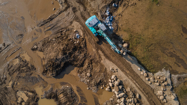 Aerial view of an excavator working on a muddy construction site with piles of rocks and earth in Karanglewas, Central Java, Indonesia.