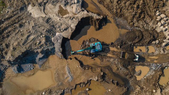 Aerial view of an excavator working in a muddy quarry with excavated earth and pools of water in Karanglewas, Central Java, Indonesia.