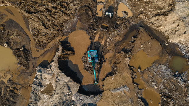 Aerial view of an excavator working in a muddy quarry with earthworks and heavy machinery in Karanglewas, Central Java, Indonesia.