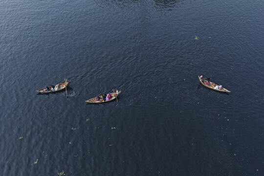 Dhaka, Bangladesh - 23 January 2026: Aerial view of three small wooden boats carrying people on the dark water of the Buriganga River.