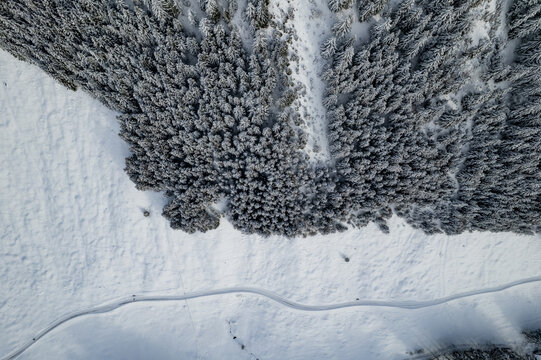 Aerial view of Dienersberger Weg winding through a snow-covered forest and open fields in Oberstdorf, Bayern, Germany.