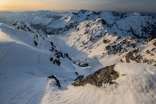 View of Temne Smreciny valley covered in snow as seen from the rocky slopes of Koprovsky stit during golden hour in Vysoke Tatry, Presov Region, Slovakia.