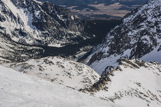 Aerial view of Mengusovska dolina with the frozen Popradske pleso tarn surrounded by snow-covered rocky peaks and pine forests in Vysoke Tatry, Presovsky kraj, Slovakia.