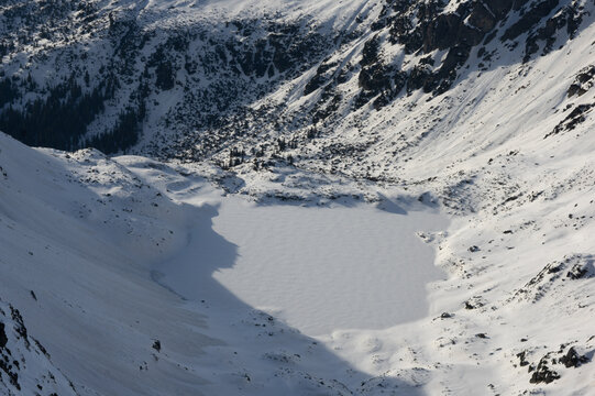 View of the frozen Temne Smreciny lake nestled within the snow-covered peaks of the High Tatras mountains, captured from the heights of Koprovsky stit in Vysoke Tatry, Presov Region, Slovakia.