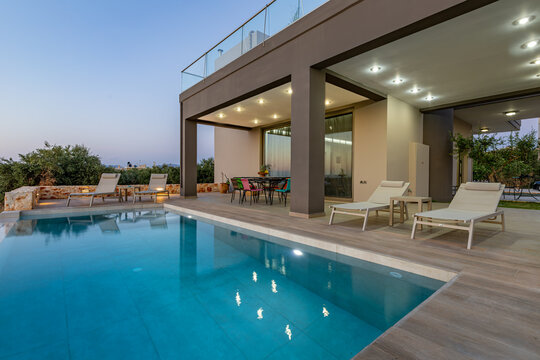 View of a modern villa with a private swimming pool, sun loungers, and outdoor dining area at dusk in Chania, Greece.