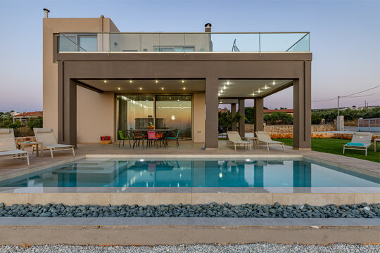 View of a modern villa with a swimming pool, outdoor dining area, and lounge chairs in Chania, Greece.