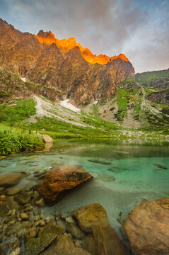 View of Zelene Kacacie pleso in Litvorova dolina with golden light on Ganok mountain peaks and turquoise water in the foreground in Tatranska Javorina, Presovsky kraj, Slovakia.