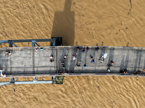 Aerial view of Jembatan Gentala Arasy with people walking across the pedestrian bridge over the muddy Batang Hari river in Kecamatan Jambi Timur, Jambi, Indonesia.