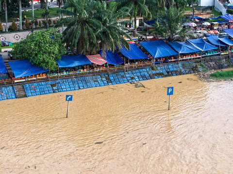 Aerial view of Jembatan Gentala Arasy area with blue tents along the muddy riverbank and parking signs in Kecamatan Jambi Timur, Jambi, Indonesia.