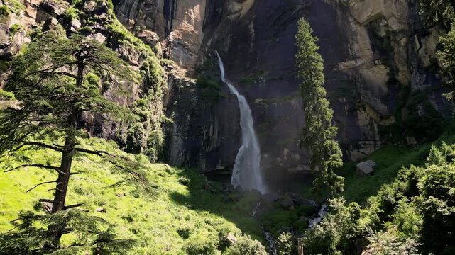 Aerial view of Jogini Falls cascading down a rocky cliff surrounded by lush green pine forests in Manali, Himachal Pradesh, India.