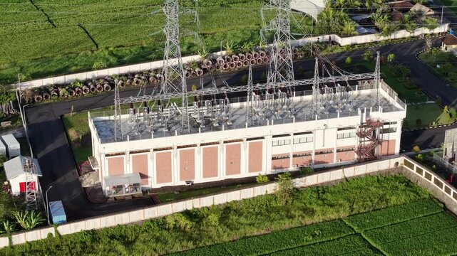 Aerial view of GIS Tanah Lot electrical substation surrounded by green rice fields in Kecamatan Kediri, Bali, Indonesia.