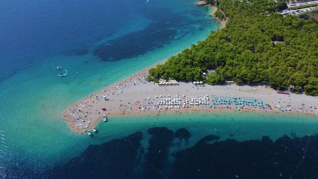 Aerial view of the iconic Golden Horn Beach with turquoise waters, pine forests, and beach umbrellas on the shore in Bol, Split-Dalmatia County, Croatia.