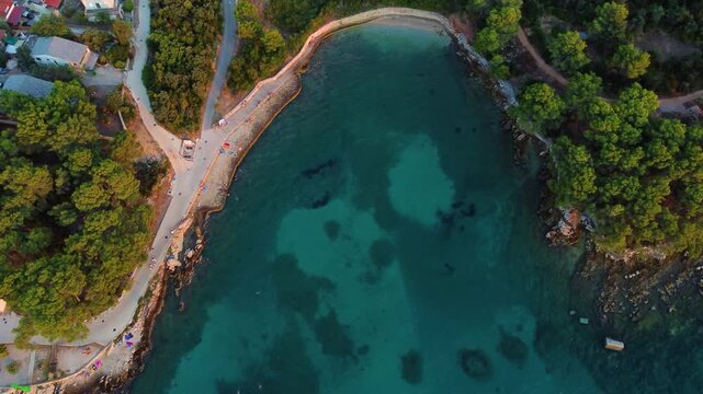 Aerial view of the turquoise waters of Beach Lanterna, pine forests, and a coastal walking path in Stari Grad, Croatia.