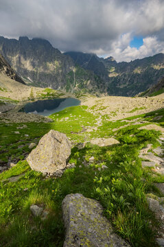 View of Litvorove pleso surrounded by rugged mountain peaks, lush green slopes, and rocky terrain under a dramatic cloudy sky in Tatranska Javorina, Presovsky kraj, Slovakia.