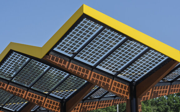 View of the Fastned Charging Station featuring its distinctive yellow roof and integrated solar panels under a clear blue sky in Arnhem, Gelderland, Netherlands.