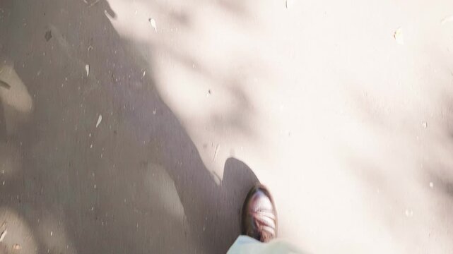 POV first person view of man in leather shoes walking on sunny pavement with shadows. Businessman or modern guy taking steps forward on asphalt road on bright day. Concept of journey and progress.