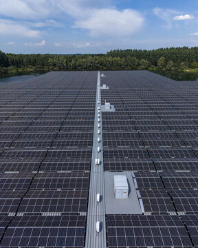 Aerial view of the De Kolk floating solar park featuring rows of photovoltaic panels on water with a central maintenance walkway surrounded by lush trees in Hattemerbroek, Gelderland, Netherlands.