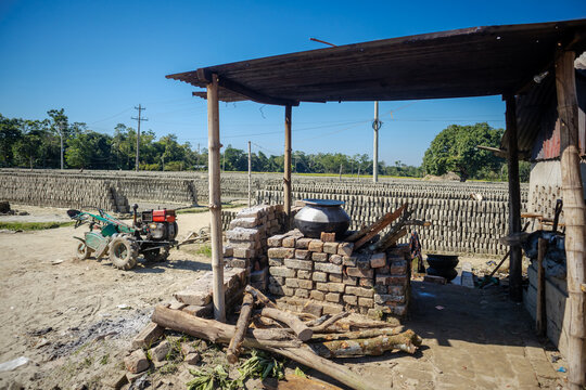 Feni, Chittagong Division, Bangladesh - 19 November 2024: View of a brick kiln site with rows of sun-dried bricks, a makeshift stove, and a small tractor under a clear blue sky.