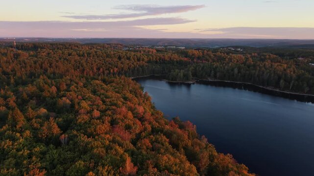 Aerial view of Stora Kasjon lake surrounded by dense autumn forests under a soft sunset sky in Ojersjo, Vastra Gotaland Count, Sweden.
