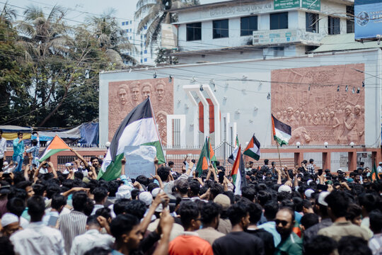 Feni, Bangladesh - 07 April 2025: View of a large crowd of protesters gathered in front of the Central Shaheed Minar monument, holding flags and signs during a demonstration.