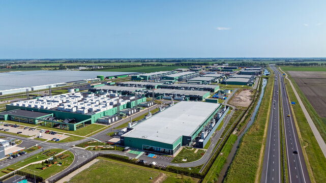 Aerial view of a large industrial data center complex with green buildings, white rooftops, and parking lots situated near a highway in Middenmeer, North Holland, Netherlands.