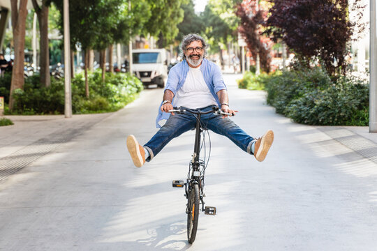 Funny senior man riding bicycle in urban city having fun during active lifestyle. Happiness, vitality and retirement