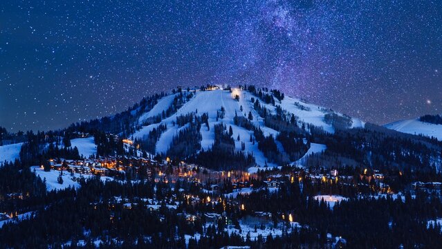 Aerial view of Deer Valley ski resort at night with illuminated lodges nestled in snow-covered mountains under a starry sky in Park City, Utah, United States.