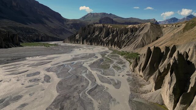 Aerial view of Spiti Valley featuring a winding river bed, dramatic jagged rock formations, and towering mountains under a clear blue sky in Lahaul and Spiti, Himachal Pradesh, India.