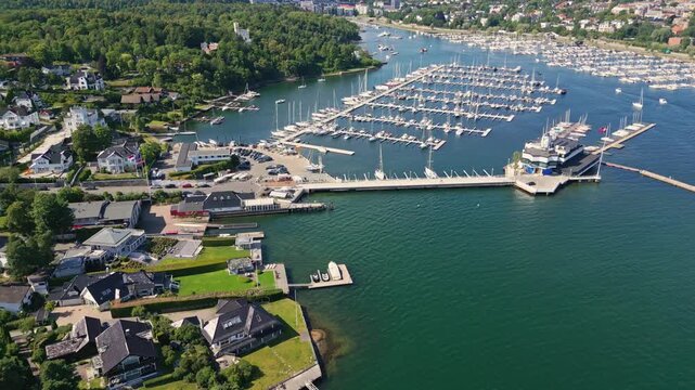 Aerial view of the Bygdoy marina featuring numerous yachts and boats docked in the calm waters of the fjord surrounded by lush green residential areas in Oslo, Oslo, Norway.