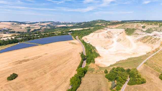 Aerial view of a limestone quarrying operation alongside a large solar panel field in a rural landscape with golden fields and a road in Grevenmacher, Grevenmacher, Luxembourg.