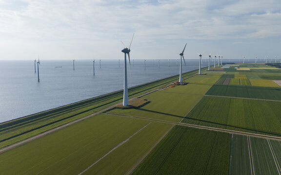 Aerial view of wind turbines standing in the water along the green agricultural fields of the polder landscape in Espel, Flevoland, Netherlands.