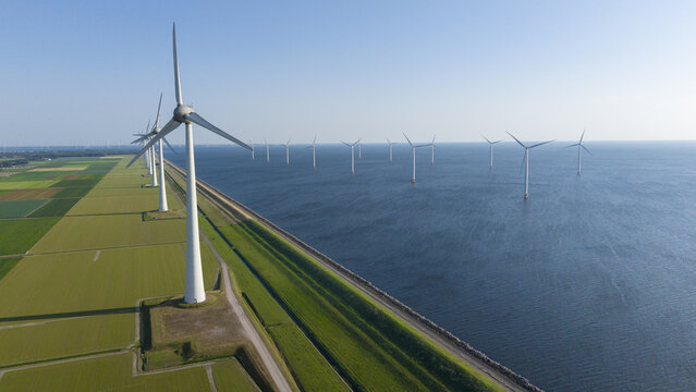 Aerial view of a wind farm with turbines standing in the water and along the green coastline in Espel, Flevoland, Netherlands.