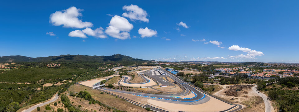 Alcabideche, Portugal - 16 July 2026: Aerial view of Autodromo Fernanda Pires da Silva race track with asphalt curves, blue curbing, surrounding green hills, and clear blue sky.