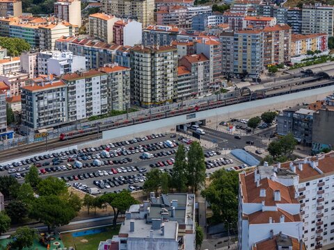 Aerial view of the Cacem train station area with a train on the tracks, a large parking lot filled with cars, and surrounding residential buildings in Agualva-Cacem, Lisbon, Portugal.