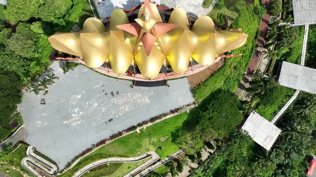 Aerial view of the golden Menara Siger landmark surrounded by lush tropical greenery and paved plazas in Bakauheni, Lampung, Indonesia.