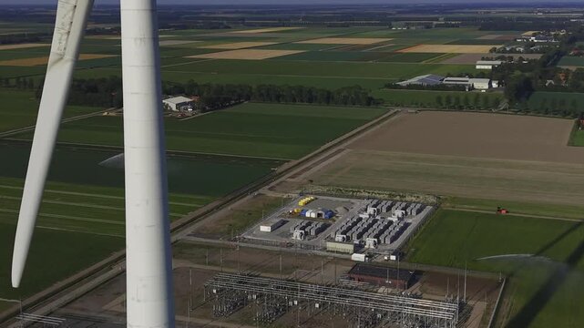 Aerial view of a large wind turbine and a power substation surrounded by green agricultural fields in Espel, Flevoland, Netherlands.