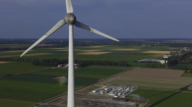Aerial view of a large wind turbine standing amidst agricultural fields and an electrical substation in Espel, Flevoland, Netherlands.