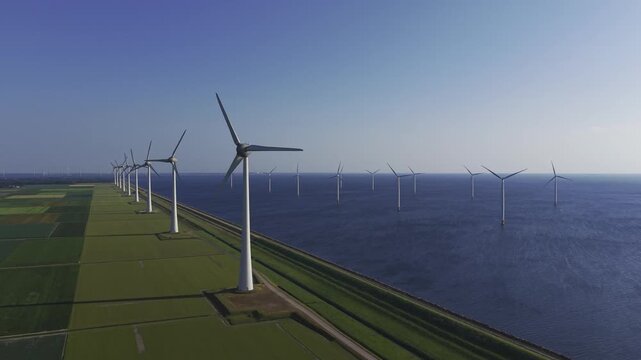 Aerial view of Windpark Noordoostpolder with rows of wind turbines standing in the water along the green coastline of IJsselmeer, Flevoland, Netherlands.