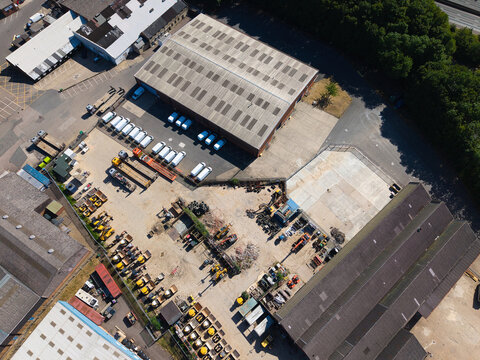 Aerial view of an industrial construction site featuring a large warehouse, rows of parked white vans, and various heavy construction machinery in Lutterworth, England, United Kingdom.
