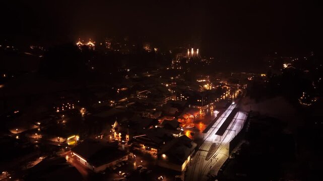 Aerial view of illuminated Gstaad village at night with glowing buildings and railway station in Saanen, Bern, Switzerland.