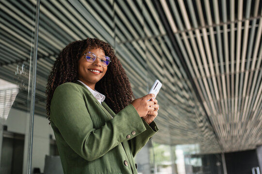 Smiling African American business woman standing in the office using mobile phone